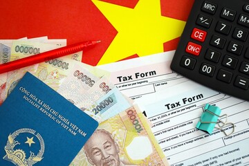 Vietnamese dong money bills and calculator with tax form on flag. Taxation and accounting concept