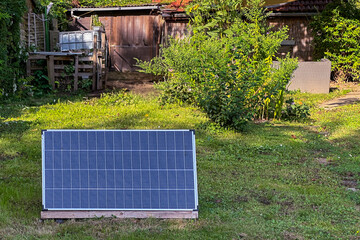Solar panel in front of old abandoned rustic house in overgrown garden