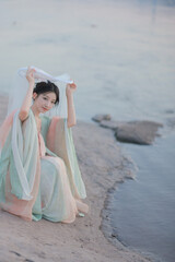 Serene young woman in pastel attire by the water's edge.