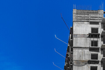 Wall load-bearing floors of multi-storey building during construction, used by pouring liquid concrete into removable formwork inside, mounting steel reinforcing cage. Blank clear blue sky copy space