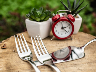Red alarm clock and forks on wooden slab