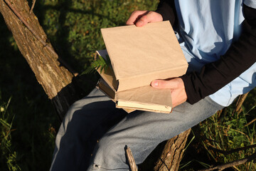 A guy in jeans and a blue T-shirt reads a hardcover book while sitting on the grass.