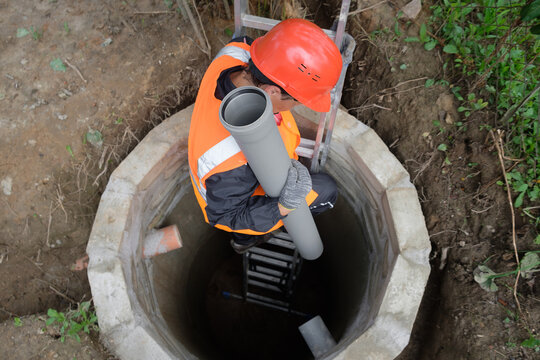 Worker in protective gear installing and inspecting septic system pipes inside a manhole at a private house, ensuring proper drainage, maintenance, and local wastewater management	