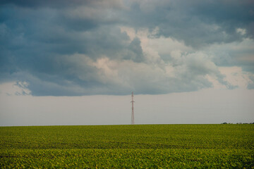 Wide shot of a flat green field under a heavy, grey cloudscape, with a lonely lattice tower...