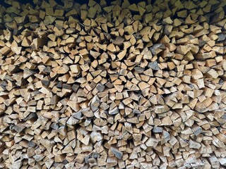 Close-up image of a neatly stacked firewood pile, showcasing cut logs arranged for efficient storage. The wood's natural texture and pattern provide a rustic appearance.