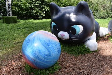 Giant black cat sculpture playing with a colorful planet ball outdoors  