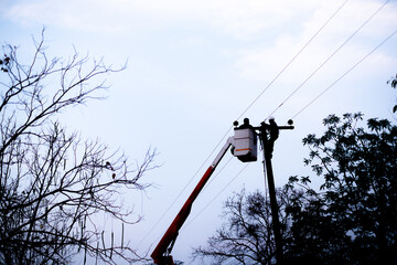 Silhouette of electrical workers repairing power lines on a utility pole using a bucket truck at dusk, ensuring maintenance and safety of electricity supply.