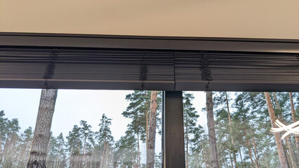 Motorized wooden blinds are folded up on a large window. Black wood automatic shutters, close-up...