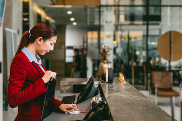 Hotel receptionist in red blazer prepares guest materials behind the front desk, focused and...