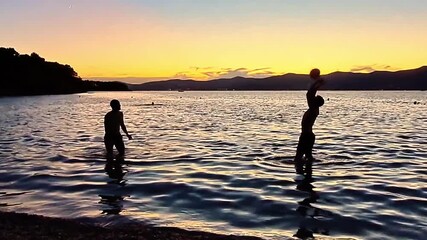 Friendship and active summer vacation. Two friends are silhouetted playing volleyball in the ocean at dusk.