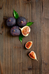Purple ripe figs fruit and slices with green leaves top view on a wooden background