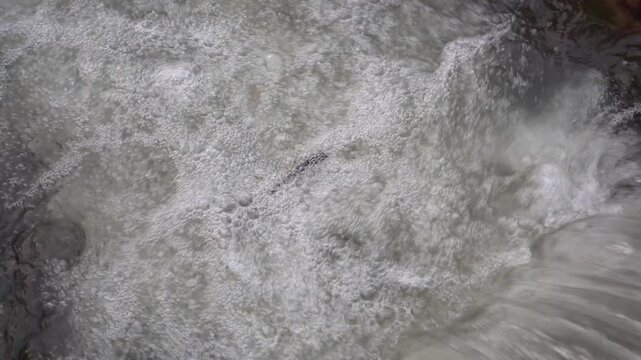 The swift, clear flow of the mountain river flows between rocks, churning with captivating white foam. The sound of the rushing air creates a calming and refreshing natural atmosphere.