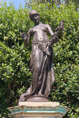 Obraz premium Statue of topless woman made of bronze in English garden in summer on plinth