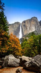 Obraz premium Majestic waterfall cascading down granite cliffs in autumnal forest