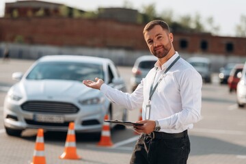 Welcome hand gesture. Driving school worker is outdoors near car
