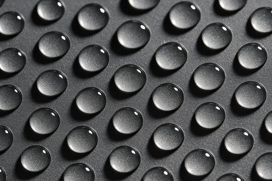 Detailed macro shot of repetitive uniform water droplets aligned in neat rows on a grey metallic surface