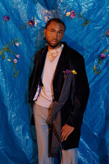 Handsome young man poses elegantly against a vibrant blue backdrop adorned with flowers