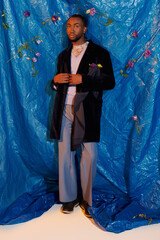 Fototapeta premium Handsome young man poses elegantly against a vibrant blue backdrop adorned with flowers
