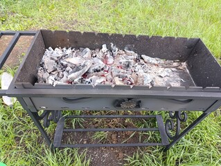 Charcoal grill with ashes and remnants in grassy outdoor setting  