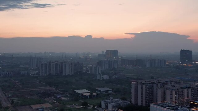 aerial drone shot flying sideways over multi story buildings in teh middle of green fields with pink orange sunset clouds overhead in gurgaon, delhi, noida, chandigarh, indore, bhopal