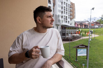 A man stands on the balcony of a hotel in a mountain village wit
