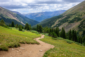 Herman Gulch path winds uphill through vibrant meadow towards a rugged Colorado Rocky Mountain. The...