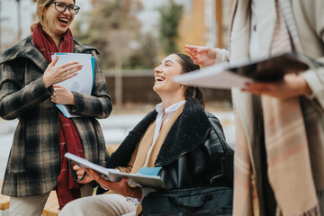 Smiling businesswomen engage in a lively conversation during an informal outdoor work gathering,...