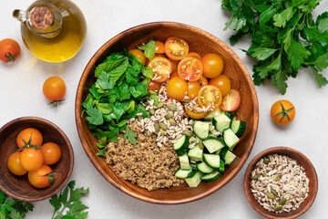 Gluten Free Quinoa Salad with Cucumber, Parsley, Mint and Yellow Cherry Tomatoes in Wooden Bowl on...