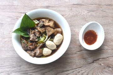 braised pork tendon and meatball with bean sprout toping fresh basil in brown soup on bowl dipping...