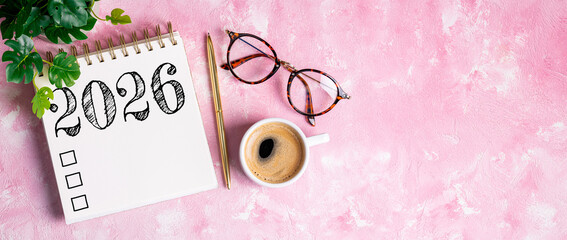 New year resolutions 2026 on desk. 2026 resolutions list with notebook, coffee cup on pink table....