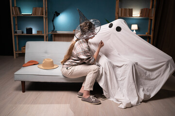 Woman in witch hat and man in Halloween costume of ghost sitting on sofa at home.