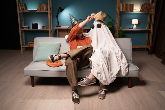 couple of friends man and woman in ghost costume celebrating halloween at home on sofa in living room. Halloween celebration - Powered by Adobe