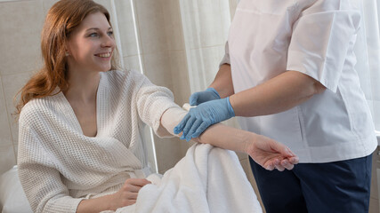 Obraz premium Young woman in bathrobe undergoing blood draw for plasmolifting in modern hospital room, health care concept