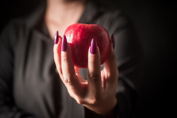 Image of a witch holding an apple in her hand, black background.