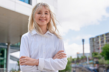Fototapeta premium Young woman smiles confidently outdoors in urban setting with modern architecture under a clear blue sky during daylight