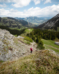Hiker in Red Jacket Descending Rocky Mountain Slope with Scenic Valley View