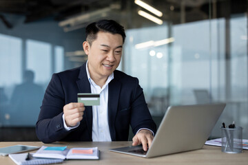 Fototapeta premium Young Asian man sitting in the office working on a laptop and using a credit card