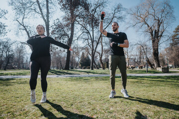A man and woman performing fitness exercises together in a public park on a sunny day, promoting...