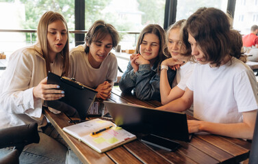 Laptop and documents are on the table. Group of young friends are in the cafe restaurant
