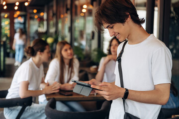 Guy is holding digital tablet. Group of young friends are in the cafe restaurant