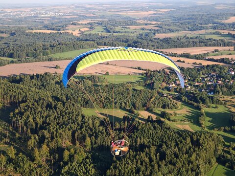 Panoramic aerial view of landscape taken from motorized paraglider, showing open terrain, fields, hills, and wide horizon under clear or partly cloudy sky.