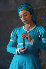 Black-haired woman in vibrant blue medieval gown and dramatic headscarf, historical elegance