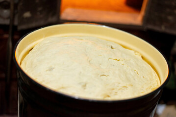 Rising yeast dough in enamel pot near traditional wood-fired oven