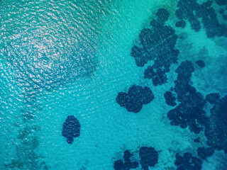 Obraz premium Turquoise water surface with dark seabed formations visible from above, creating a beautiful contrast of colors in a tropical paradise