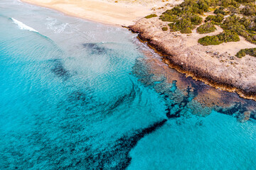 Aerial view of turquoise water gently splashing rocky coast of beach