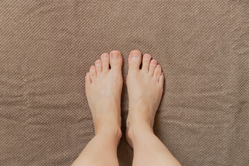 Clean female feet after washing stand on a brown towel on the floor, hygiene and foot care