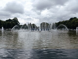 Urban fountain spraying water in city park under cloudy sky -  