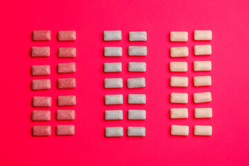 Colorful chewing gum arranged in three vertical columns on pink background

