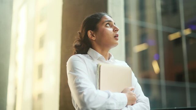 A thoughtful and focused professional is standing in a bustling urban environment, holding a notebook in hand