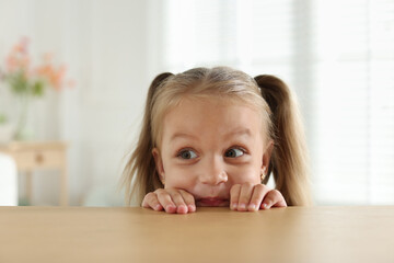 Curious little girl peeking over wooden table indoors